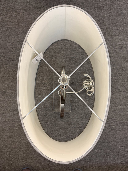 A contemporary table lamp featuring an intertwined dual-ring brushed nickel body, a clear acrylic base, and a textured gray drum shade in excellent condition.