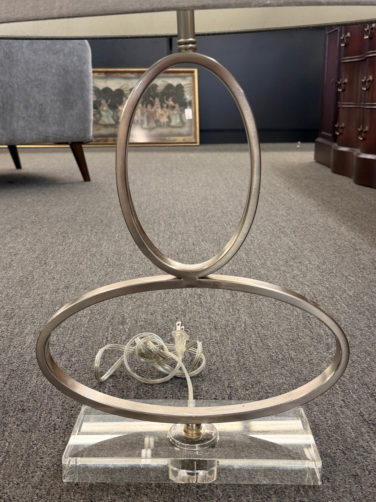 A contemporary table lamp featuring an intertwined dual-ring brushed nickel body, a clear acrylic base, and a textured gray drum shade in excellent condition.