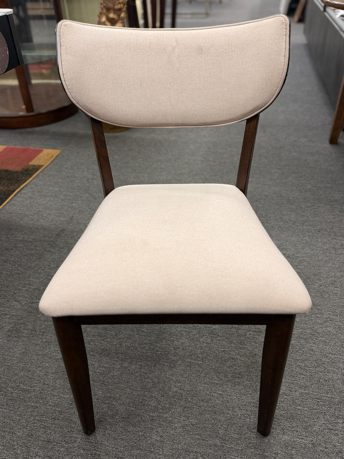 A mid-century modern dining set consisting of a round glass-top table on an angled dark-wood base paired with four curved-back off-white upholstered chairs in good condition.