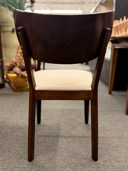 A mid-century modern dining set consisting of a round glass-top table on an angled dark-wood base paired with four curved-back off-white upholstered chairs in good condition.