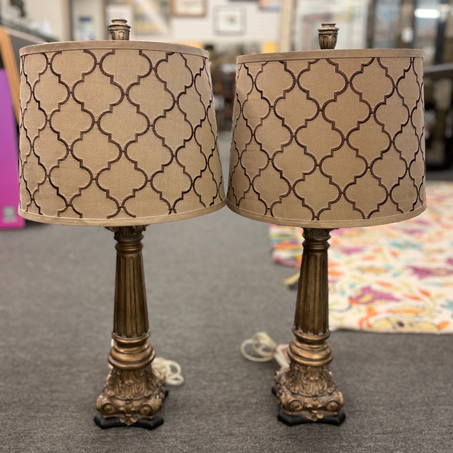A matching pair of elegant table lamps with fluted column-style antique bronze bases and tan drum shades featuring a dark brown embroidered Moroccan trellis pattern.