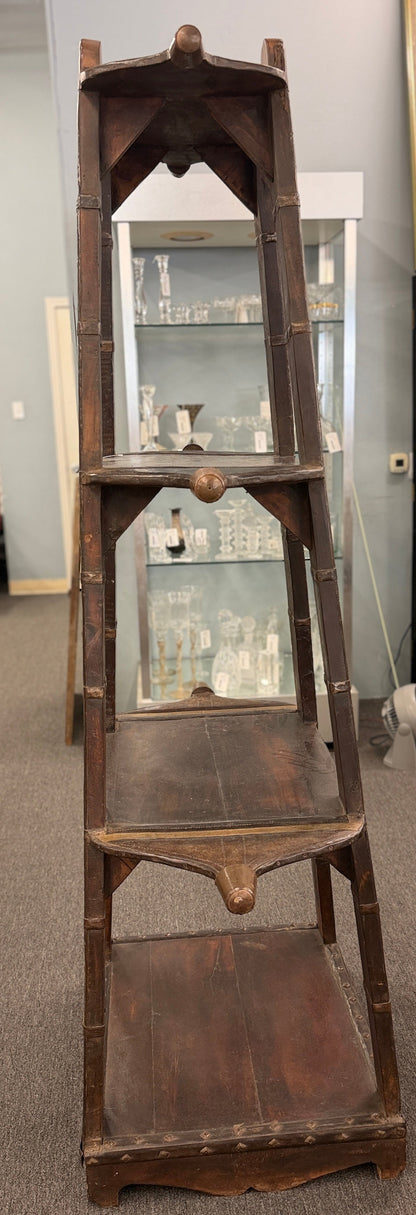 A tall, open-shelf antique-style cart bookcase with thick metal-bound wooden supports, extended carved handles, and faint gold geometric brass inlay plates.