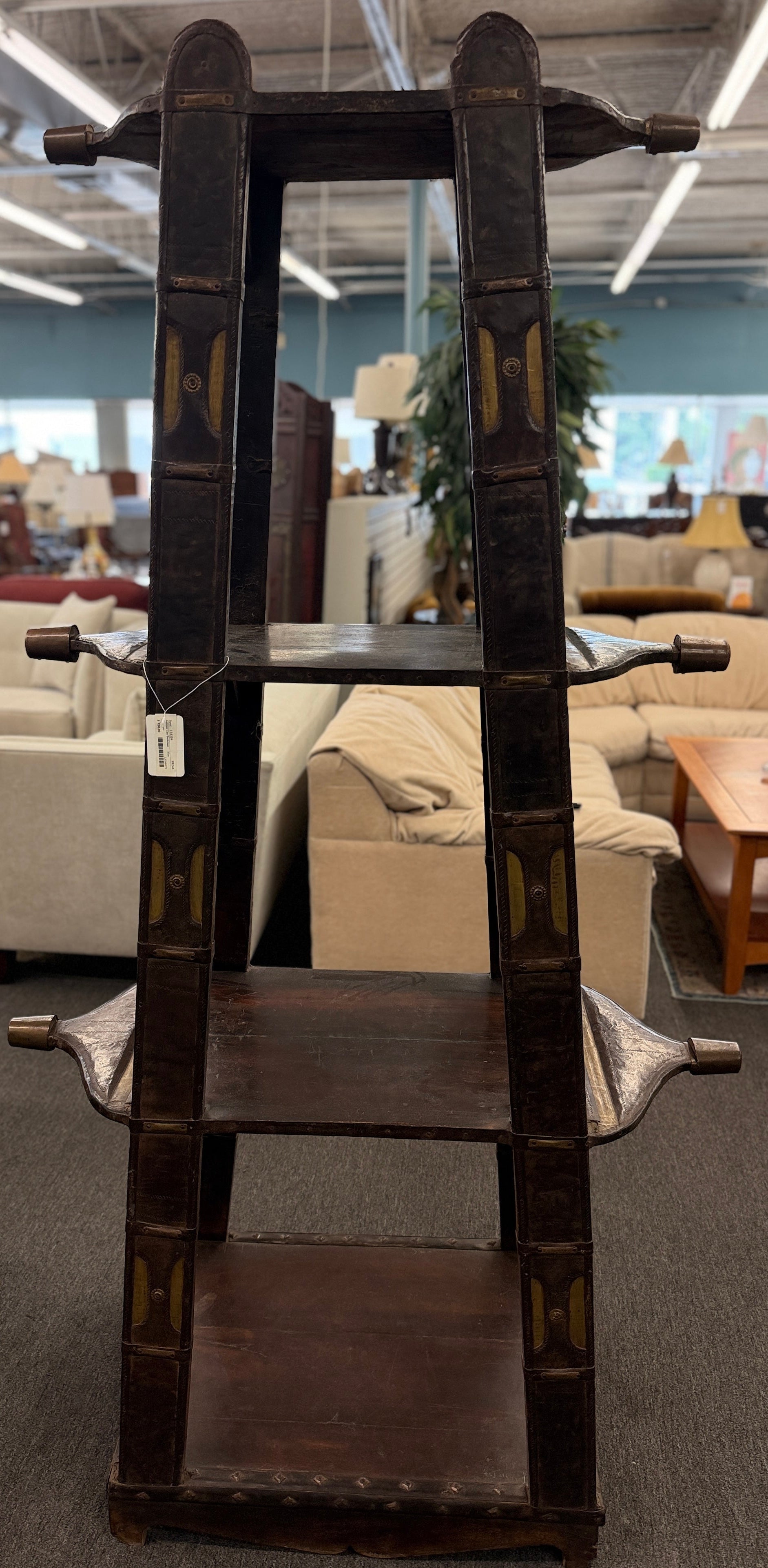 A tall, open-shelf antique-style cart bookcase with thick metal-bound wooden supports, extended carved handles, and faint gold geometric brass inlay plates.