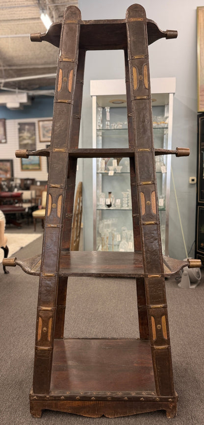 A tall, open-shelf antique-style cart bookcase with thick metal-bound wooden supports, extended carved handles, and faint gold geometric brass inlay plates.
