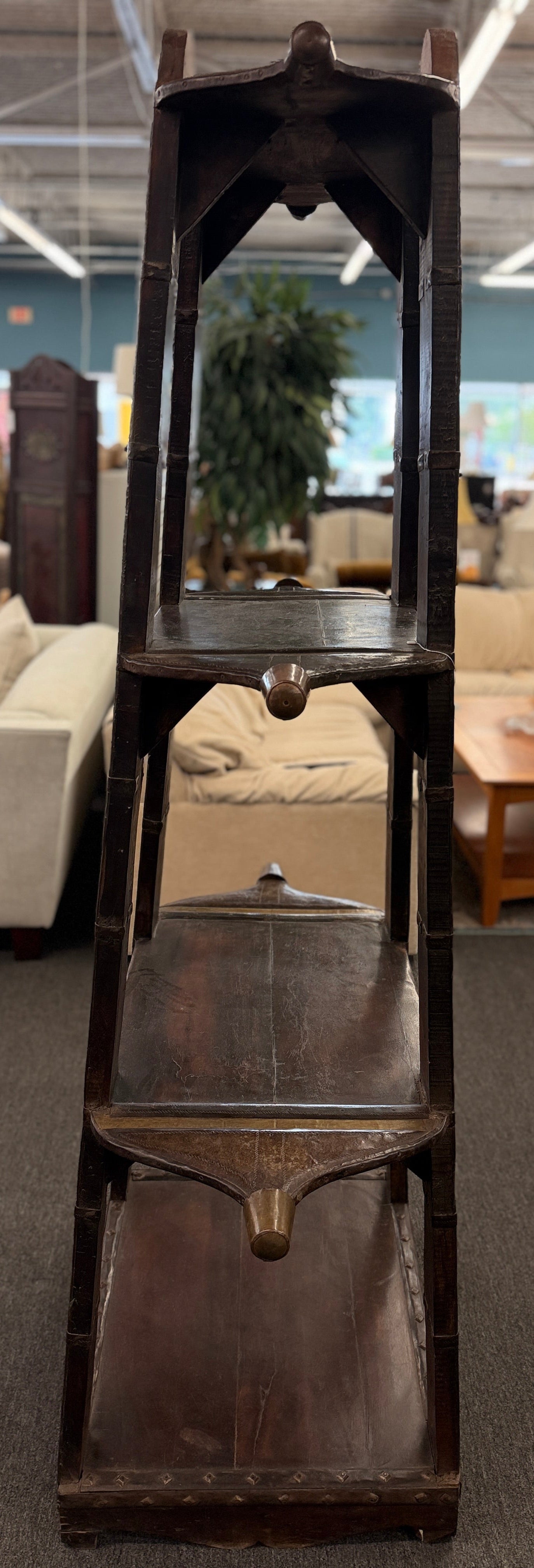 A tall, open-shelf antique-style cart bookcase with thick metal-bound wooden supports, extended carved handles, and faint gold geometric brass inlay plates.