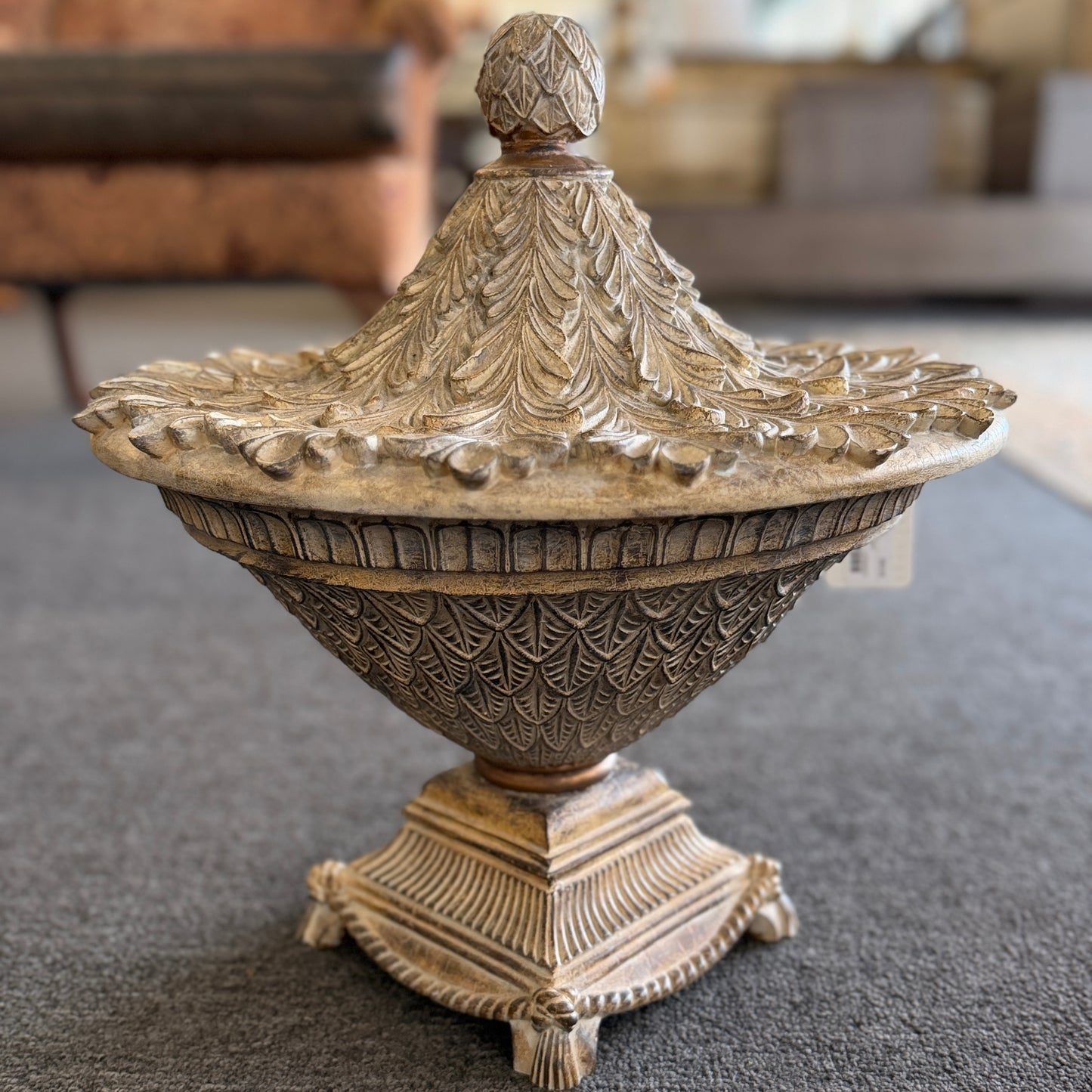 A decorative heavily textured ceramic lidded urn covered in overlapping leaf patterns with an antiqued distressed cream and brown finish.