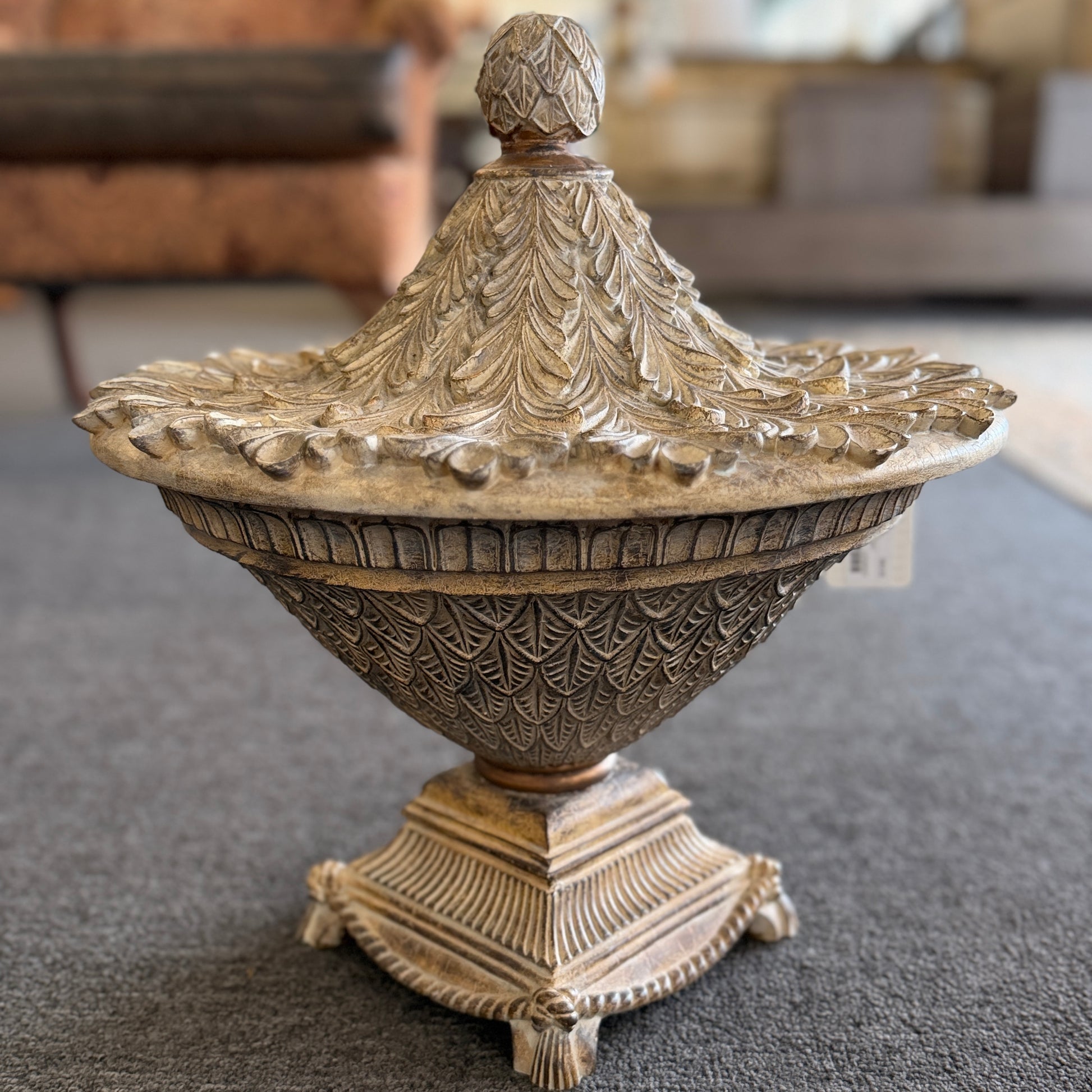 A decorative heavily textured ceramic lidded urn covered in overlapping leaf patterns with an antiqued distressed cream and brown finish.