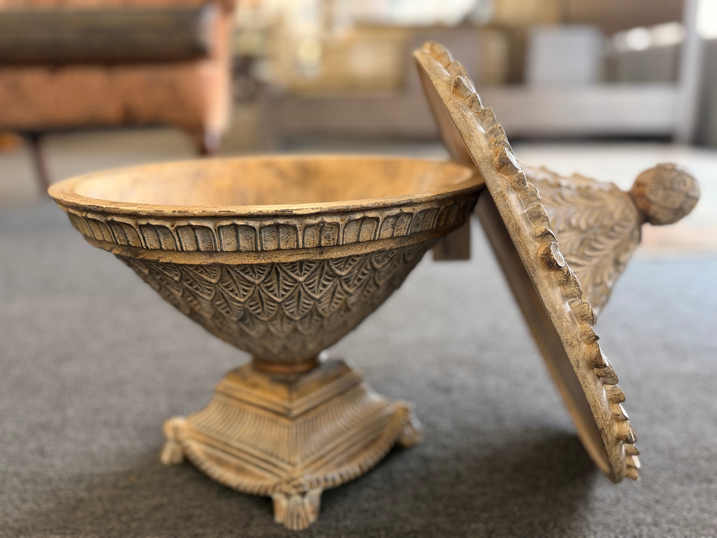 A decorative heavily textured ceramic lidded urn covered in overlapping leaf patterns with an antiqued distressed cream and brown finish.
