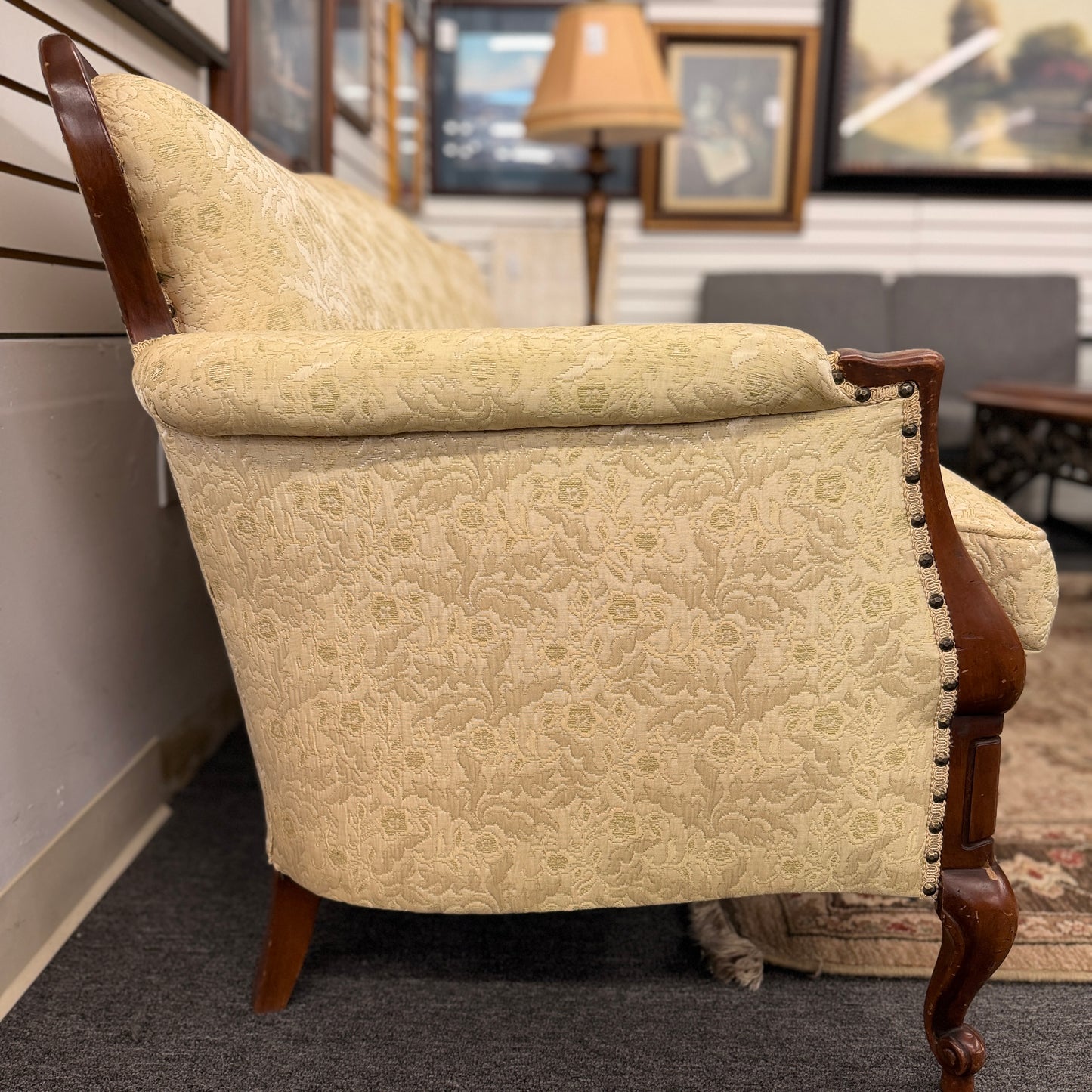 An antique camelback sofa featuring an exposed carved wood frame with floral crests, cabriole legs, and piped seat cushions.