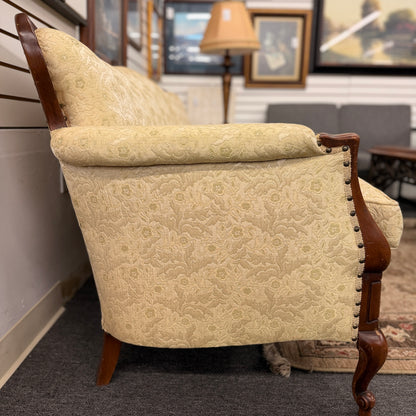 An antique camelback sofa featuring an exposed carved wood frame with floral crests, cabriole legs, and piped seat cushions.