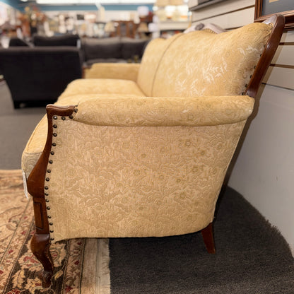 An antique camelback sofa featuring an exposed carved wood frame with floral crests, cabriole legs, and piped seat cushions.