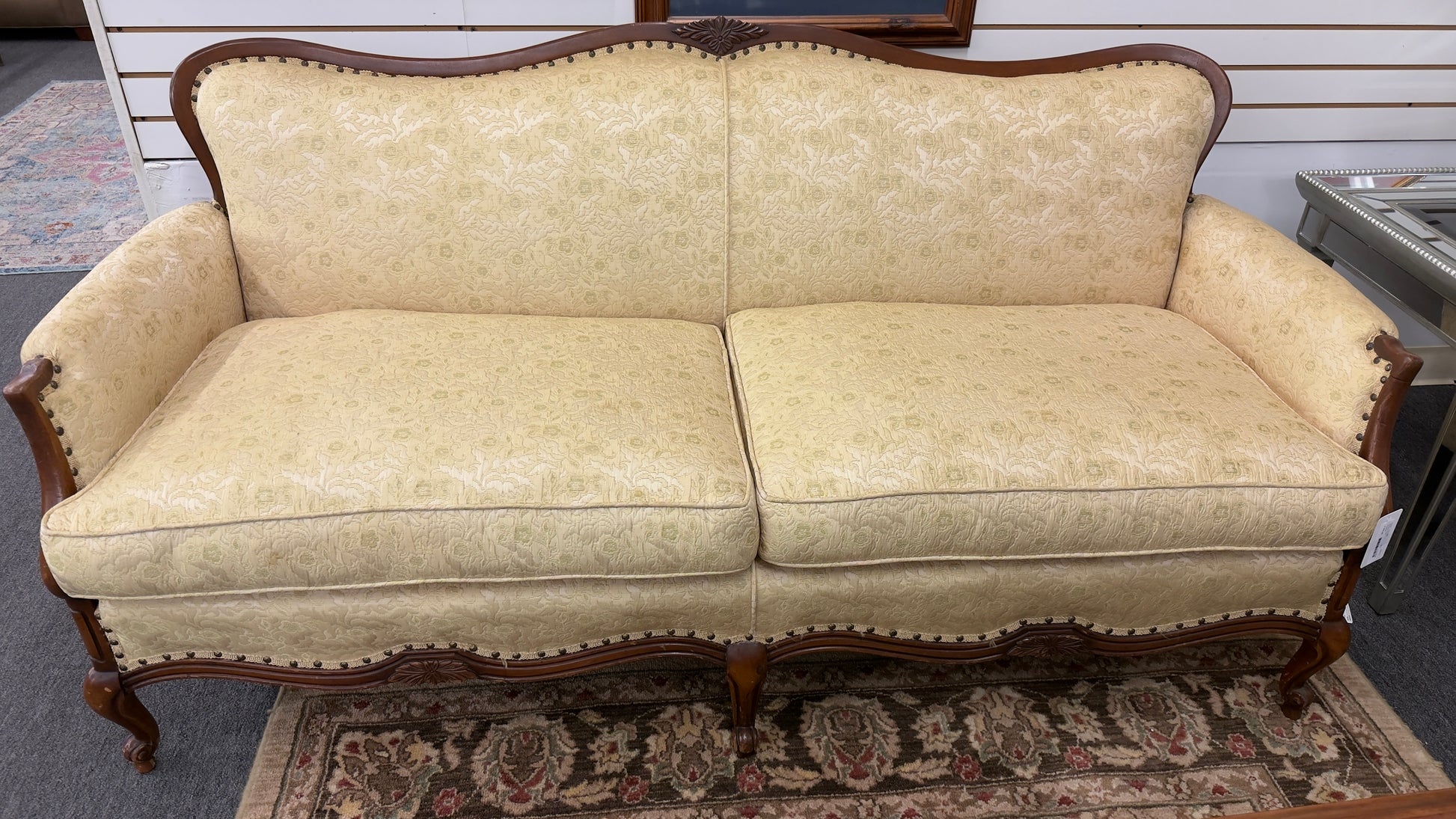 An antique camelback sofa featuring an exposed carved wood frame with floral crests, cabriole legs, and piped seat cushions.