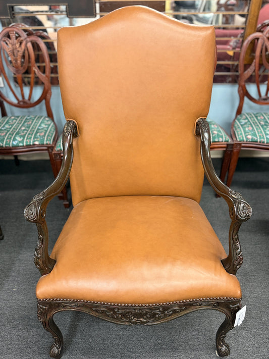 An elegant antique-reproduction accent chair upholstered in smooth tan leather with a hand-carved dark wood frame, cabriole legs, and brass nailhead trim.
