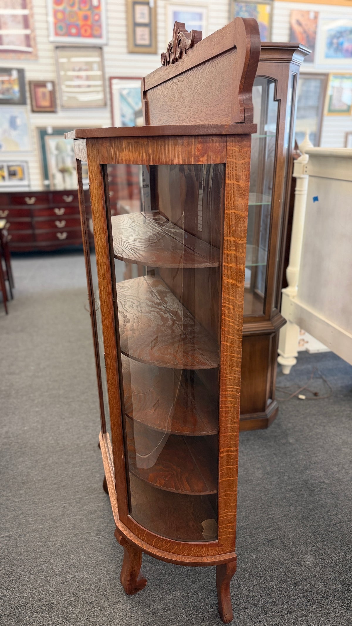 An antique-style oak curio cabinet featuring curved glass sides, an arched door with key hardware, interior shelves, and a carved pediment in good condition.