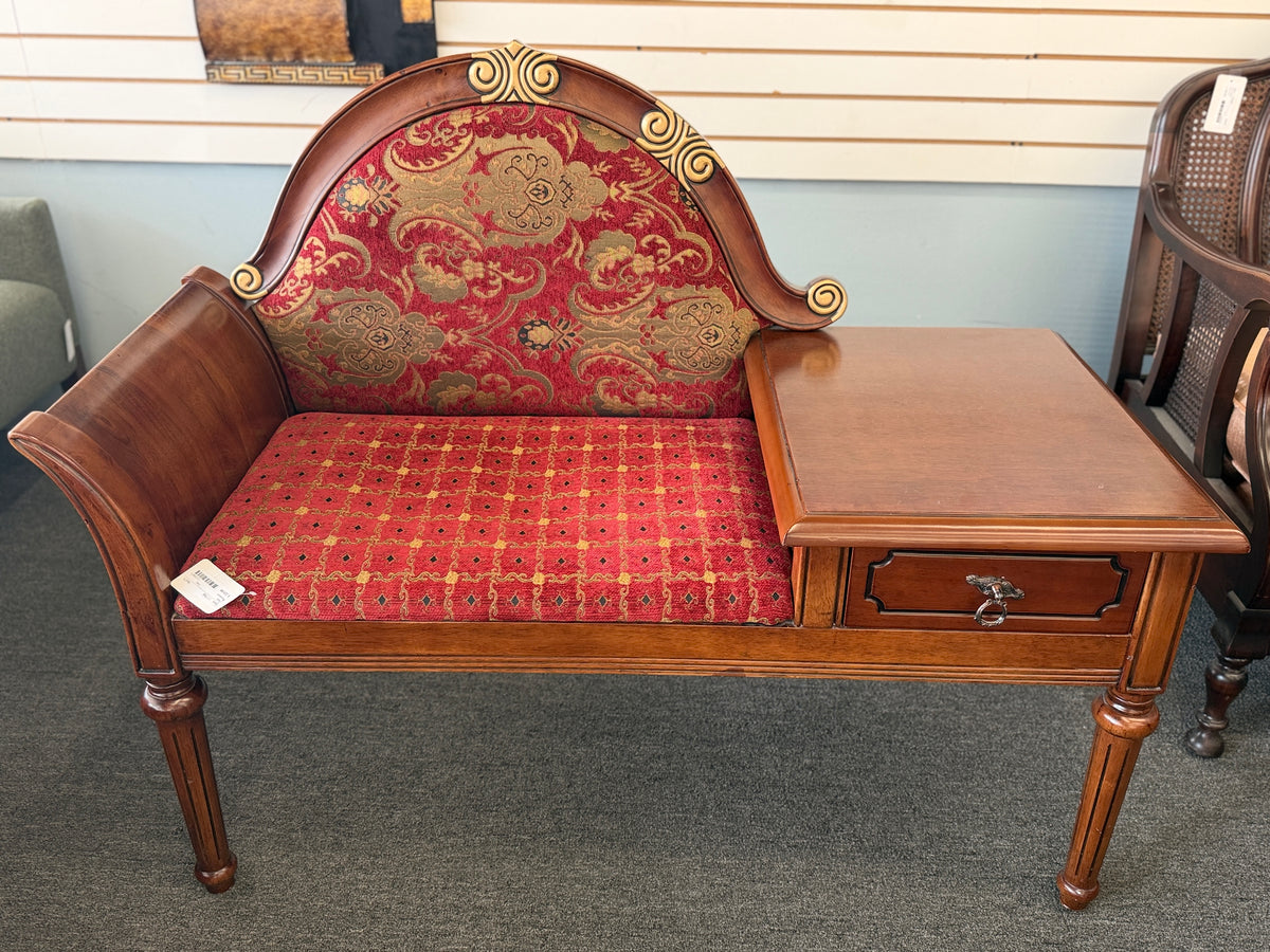 An antique-style wooden telephone chair featuring a single seat with red patterned upholstery, gold-accented scrollwork, an attached side tabletop, and a drawer in excellent condition.