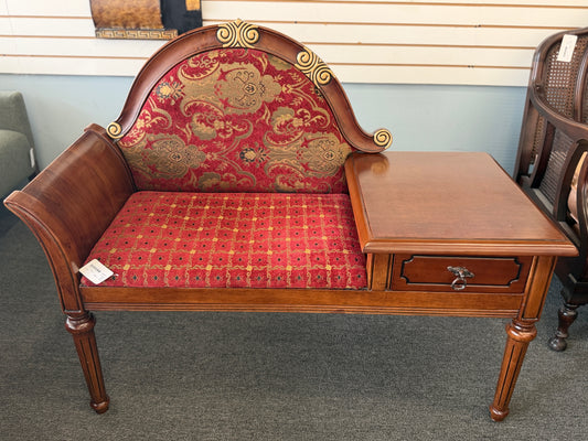An antique-style wooden telephone chair featuring a single seat with red patterned upholstery, gold-accented scrollwork, an attached side tabletop, and a drawer in excellent condition.