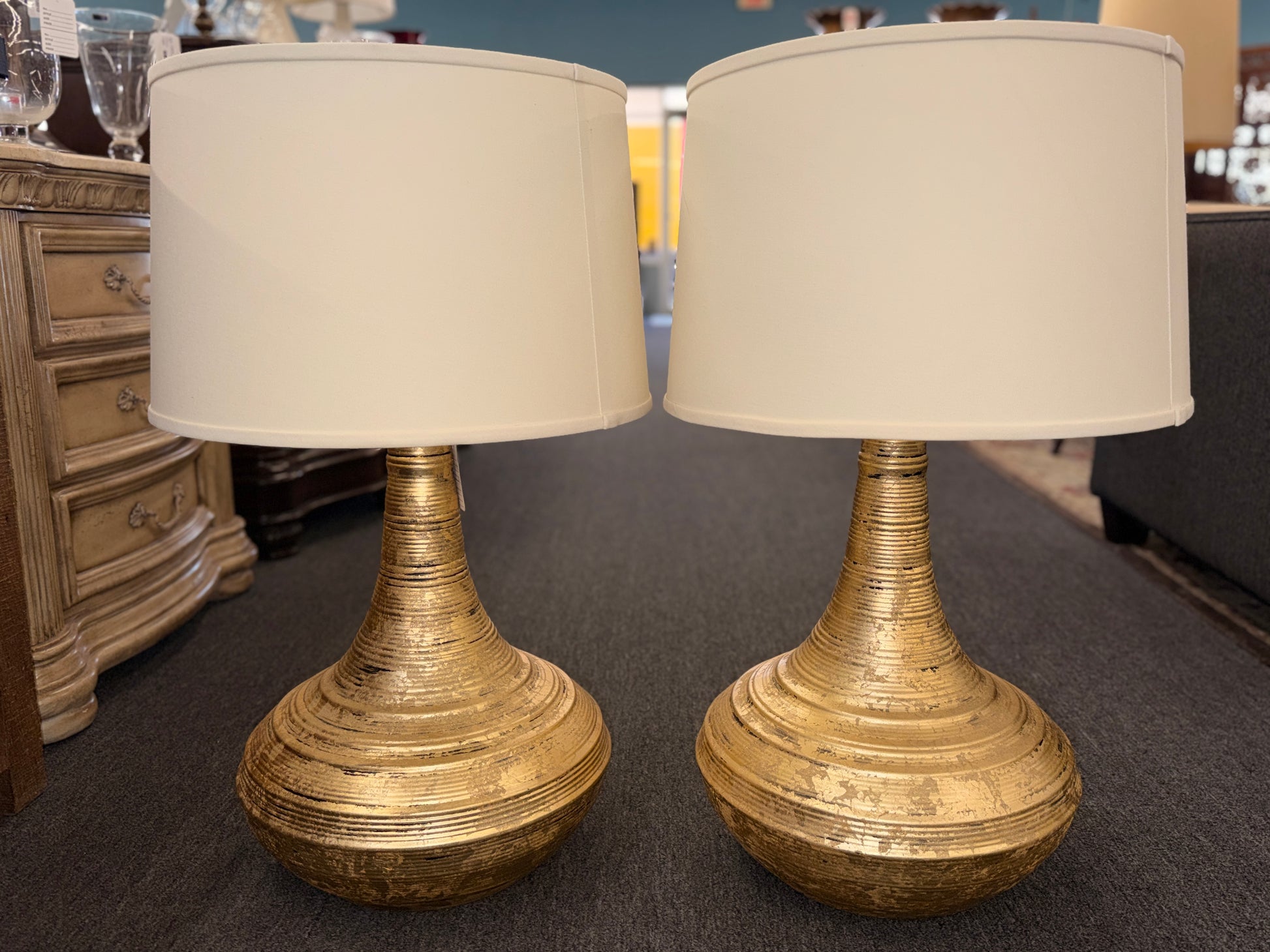 A pair of table lamps with wide teardrop-shaped bases featuring horizontal ribbing in an antiqued gold finish topped with white fabric drum shades.