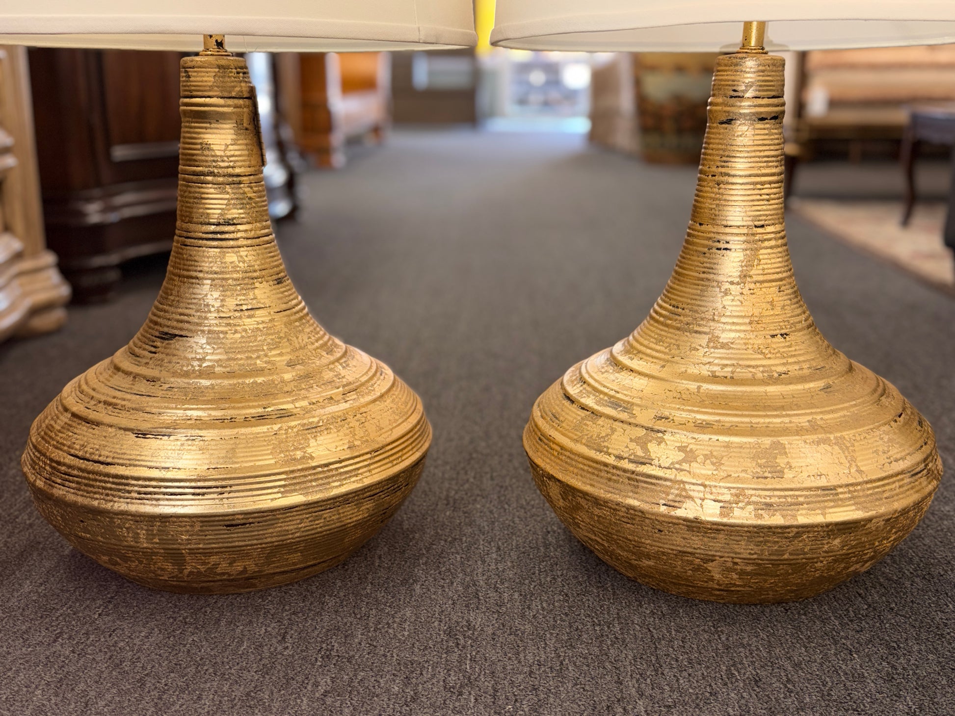 A pair of table lamps with wide teardrop-shaped bases featuring horizontal ribbing in an antiqued gold finish topped with white fabric drum shades.