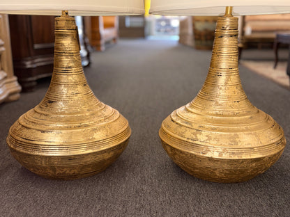 A pair of table lamps with wide teardrop-shaped bases featuring horizontal ribbing in an antiqued gold finish topped with white fabric drum shades.