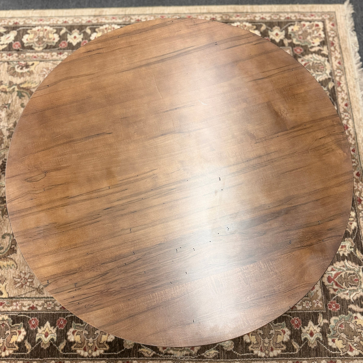 A round rustic-contemporary Bassett wooden coffee table in a warm walnut finish supported by an angular intersecting cross-base in good condition.