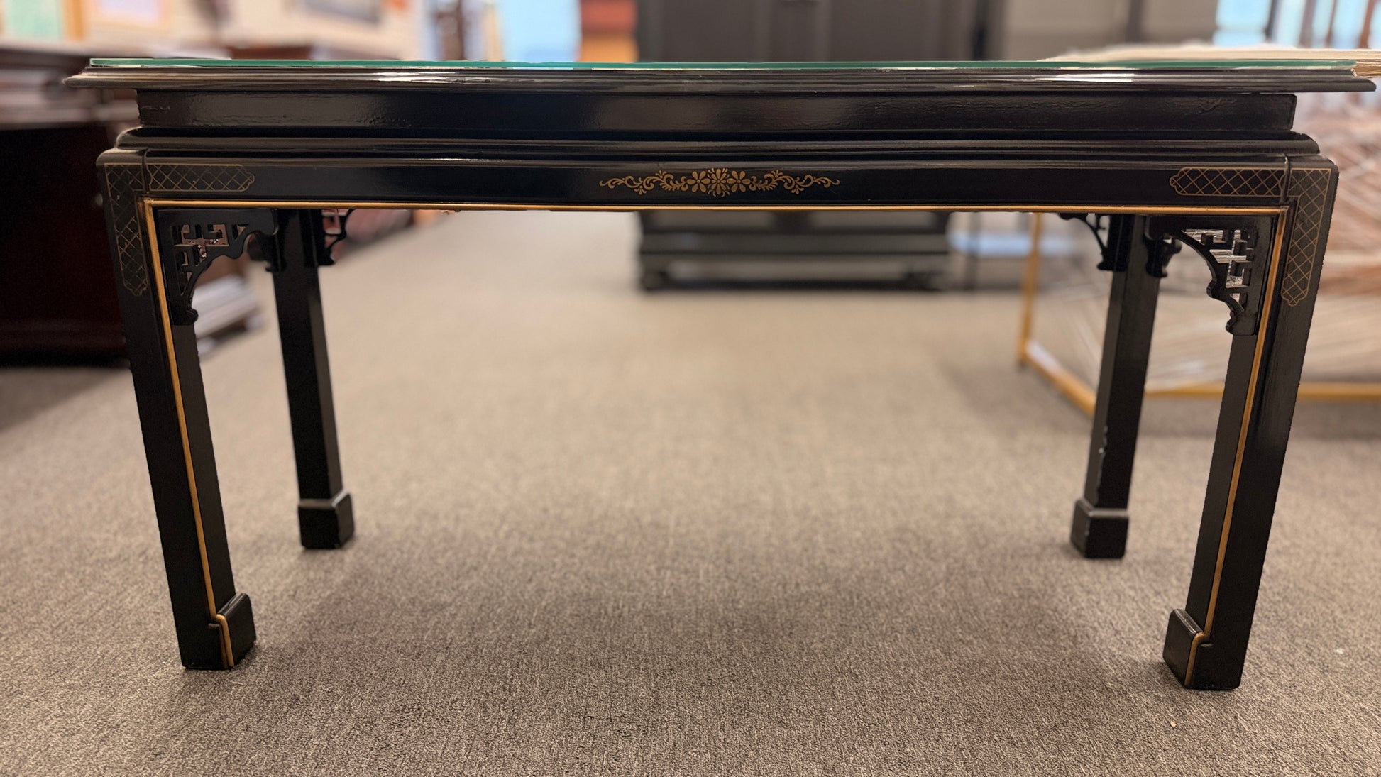 Black lacquer console table featuring hand-painted Asian-inspired scenes with figures, architecture, and landscapes beneath a protective clear glass surface.