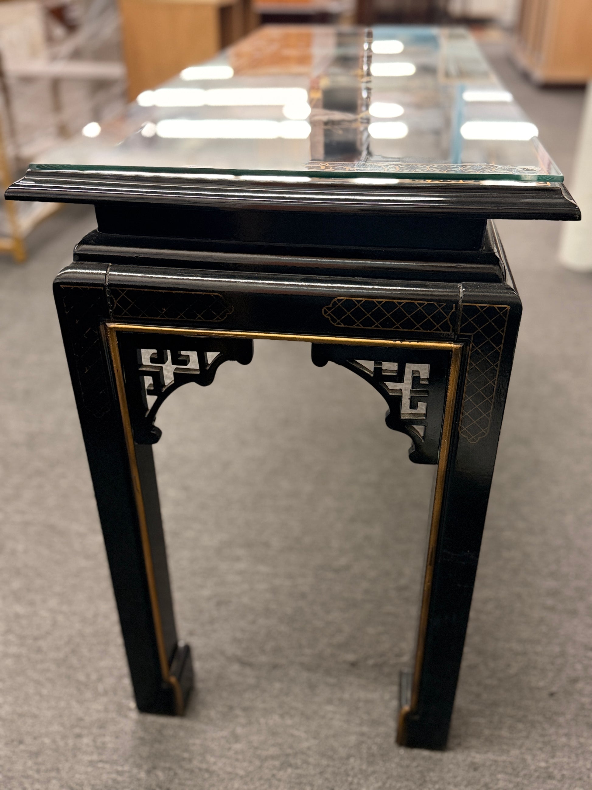 Black lacquer console table featuring hand-painted Asian-inspired scenes with figures, architecture, and landscapes beneath a protective clear glass surface.