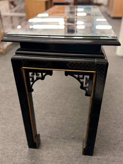 Black lacquer console table featuring hand-painted Asian-inspired scenes with figures, architecture, and landscapes beneath a protective clear glass surface.