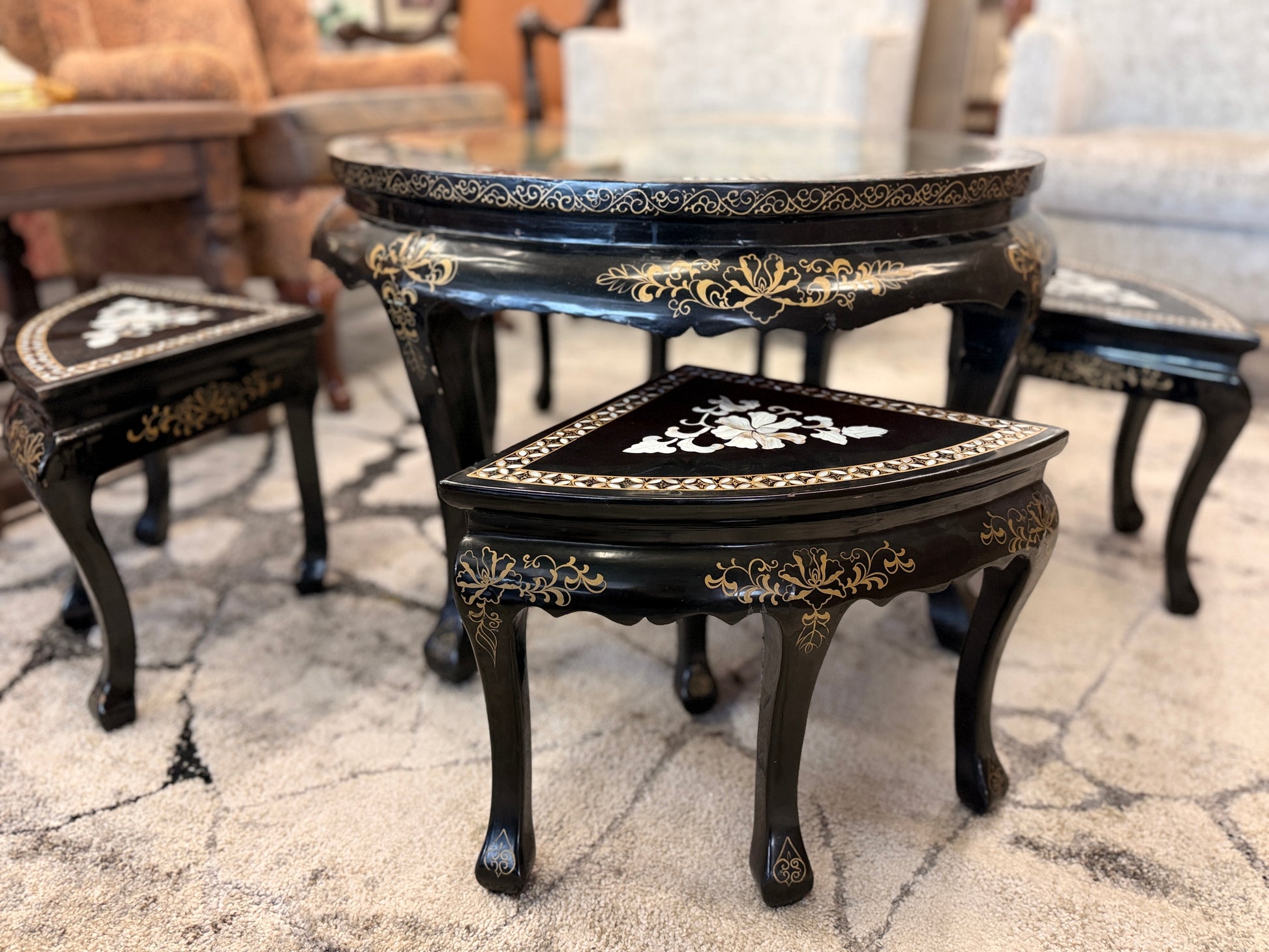 Traditional black lacquer tea table set featuring a round coffee table with a protective glass top, four triangular nesting stools, gold-painted detailing, and mother-of-pearl style floral inlays.