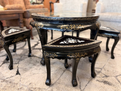 Traditional black lacquer tea table set featuring a round coffee table with a protective glass top, four triangular nesting stools, gold-painted detailing, and mother-of-pearl style floral inlays.