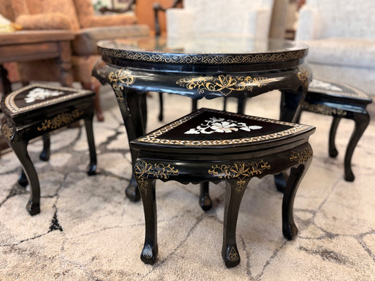 Traditional black lacquer tea table set featuring a round coffee table with a protective glass top, four triangular nesting stools, gold-painted detailing, and mother-of-pearl style floral inlays.