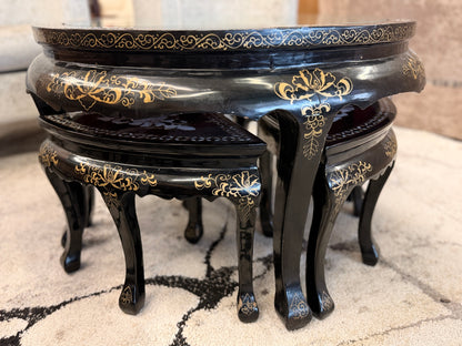 Traditional black lacquer tea table set featuring a round coffee table with a protective glass top, four triangular nesting stools, gold-painted detailing, and mother-of-pearl style floral inlays.