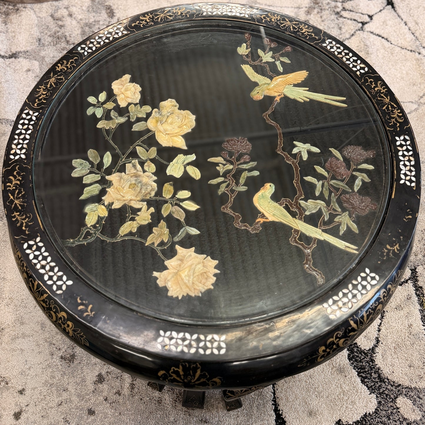 Traditional black lacquer tea table set featuring a round coffee table with a protective glass top, four triangular nesting stools, gold-painted detailing, and mother-of-pearl style floral inlays.