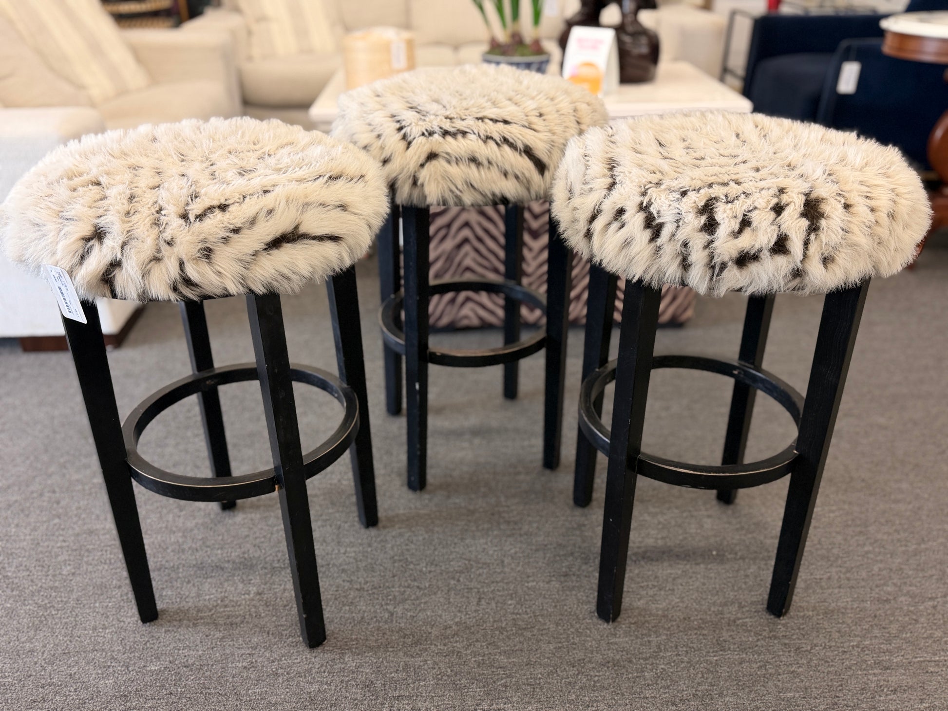 A set of three black wooden barstools featuring fluffy animal-print upholstered seats in good condition.