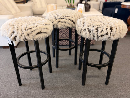 A set of three black wooden barstools featuring fluffy animal-print upholstered seats in good condition.