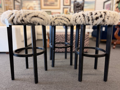A set of three black wooden barstools featuring fluffy animal-print upholstered seats in good condition.
