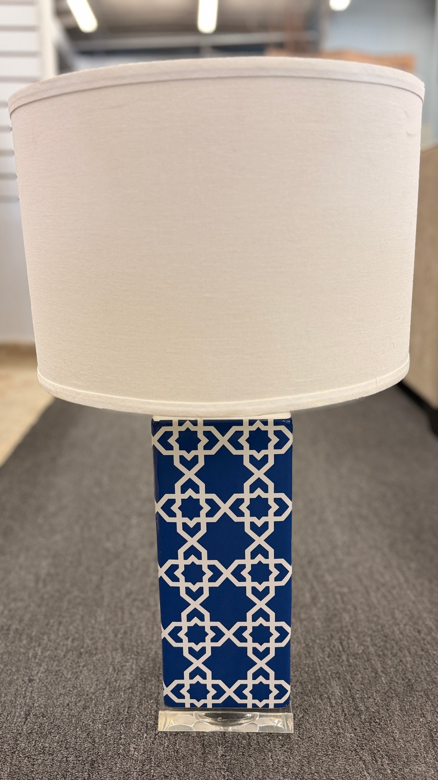 Blue and white ceramic table lamp featuring a geometric trellis pattern, rectangular column base, clear square plinth, and white fabric drum shade.