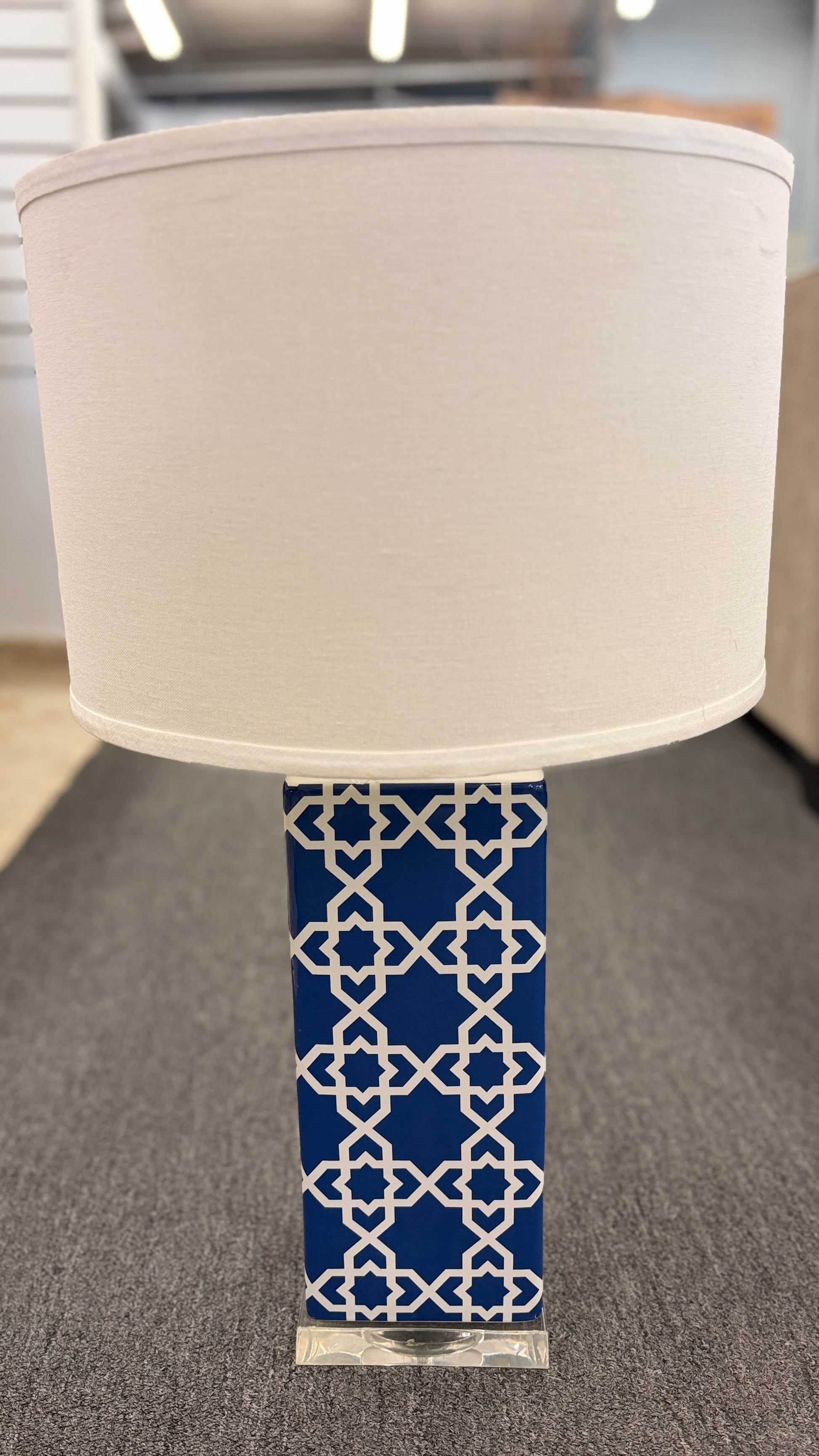 Blue and white ceramic table lamp featuring a geometric trellis pattern, rectangular column base, clear square plinth, and white fabric drum shade.