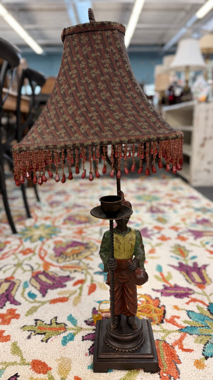 Bohemian antique style ceramic and iron table lamp featuring a unique decorative base and a fringed fabric shade on a patterned rug at 2nd Debut Houston consignment showroom