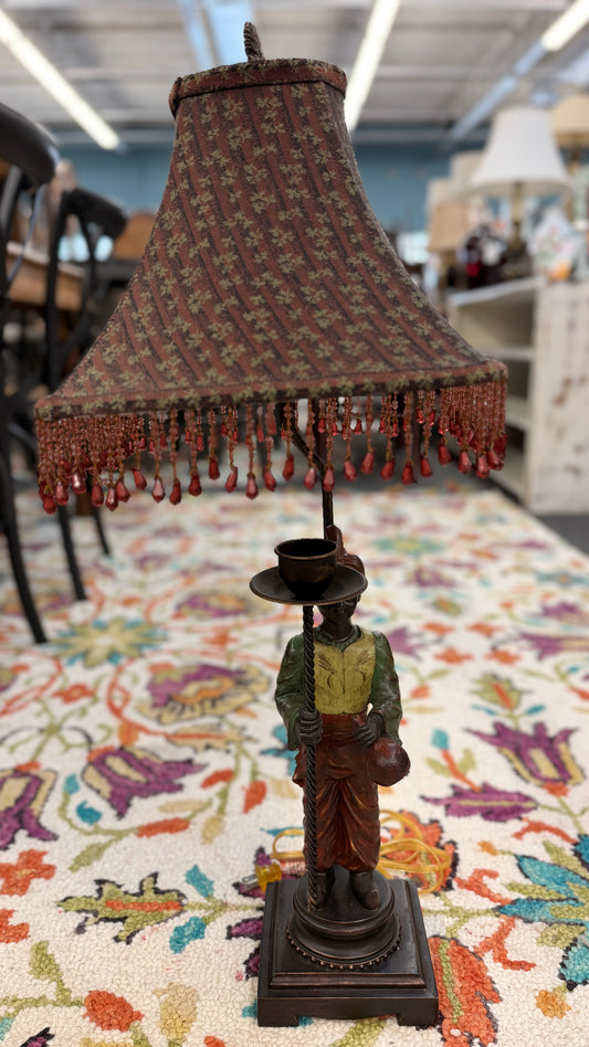 Bohemian antique style ceramic and iron table lamp featuring a unique decorative base and a fringed fabric shade on a patterned rug at 2nd Debut Houston consignment showroom