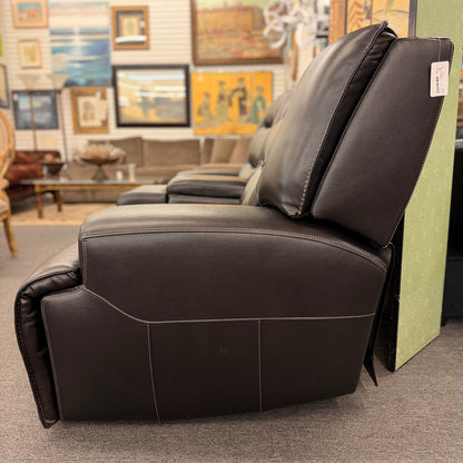 Brown dual power reclining loveseat upholstered in leather with prominent stitched detailing, independent reclining seats, and a center storage console with padded armrests.