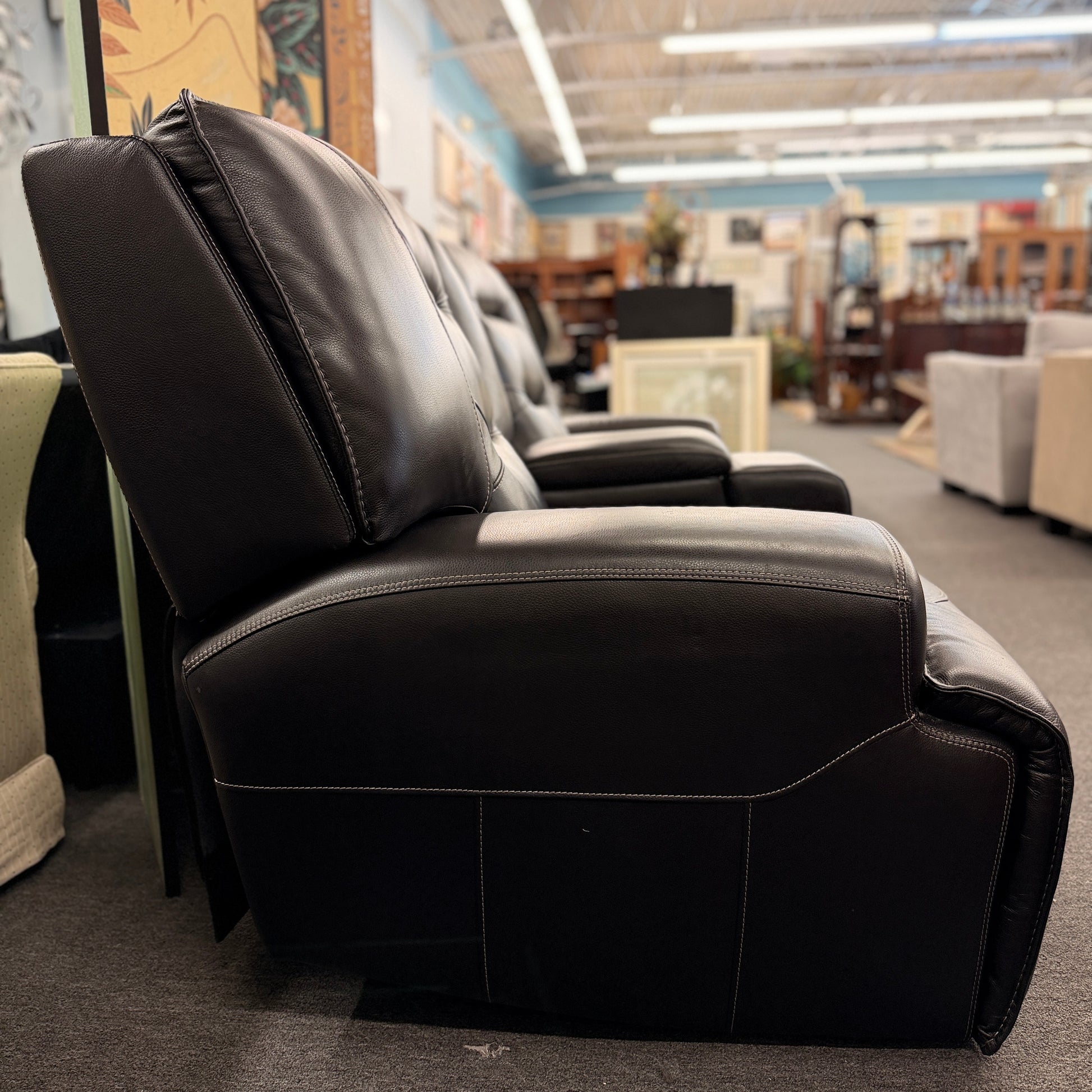 Brown dual power reclining loveseat upholstered in leather with prominent stitched detailing, independent reclining seats, and a center storage console with padded armrests.