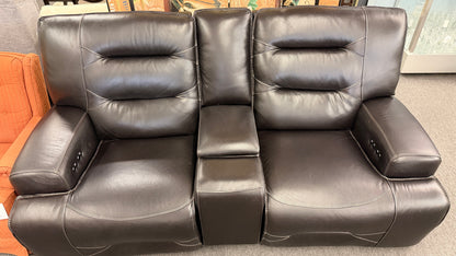 Brown dual power reclining loveseat upholstered in leather with prominent stitched detailing, independent reclining seats, and a center storage console with padded armrests.