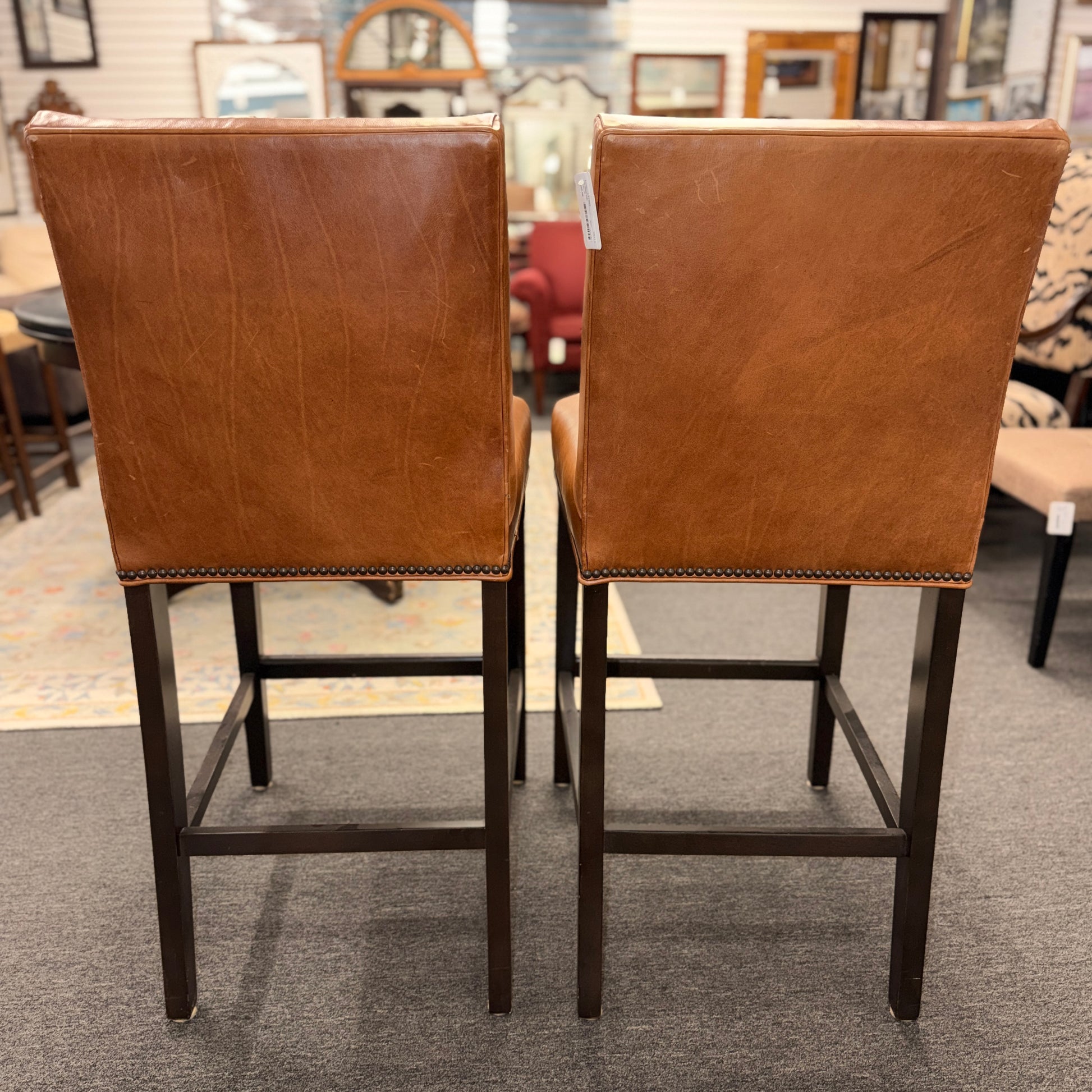 A set of two brown leather barstools featuring nailhead trim details and dark wood legs in good condition.