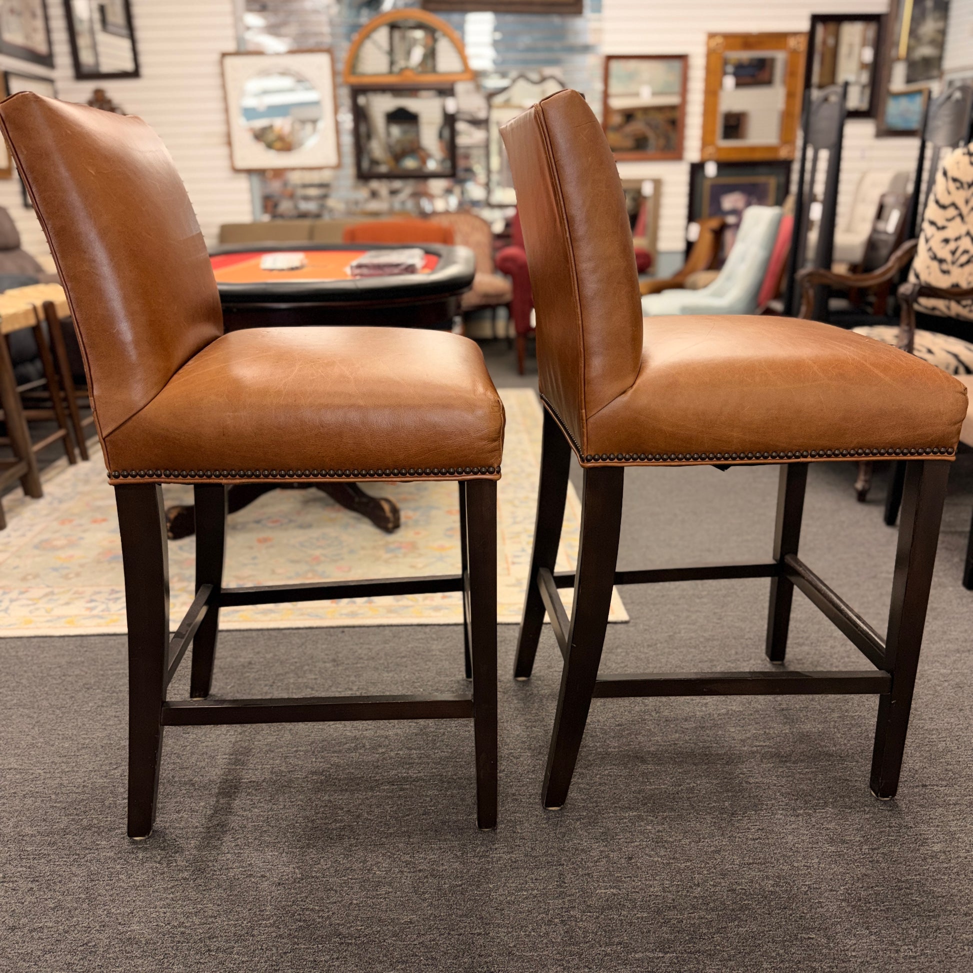 A set of two brown leather barstools featuring nailhead trim details and dark wood legs in good condition.