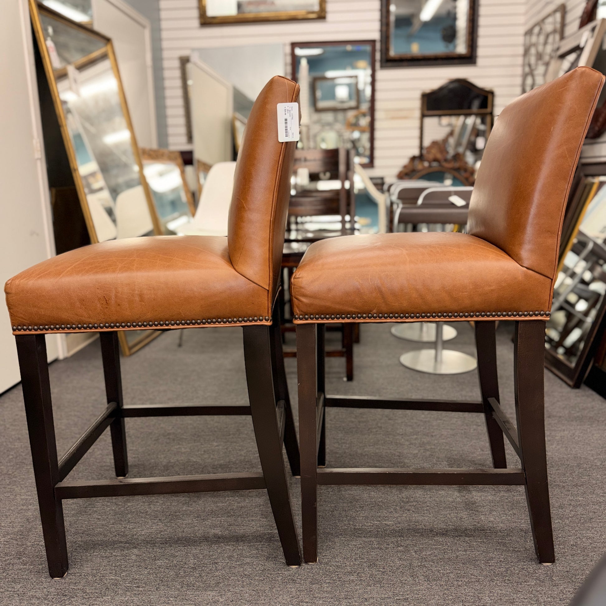 A set of two brown leather barstools featuring nailhead trim details and dark wood legs in good condition.