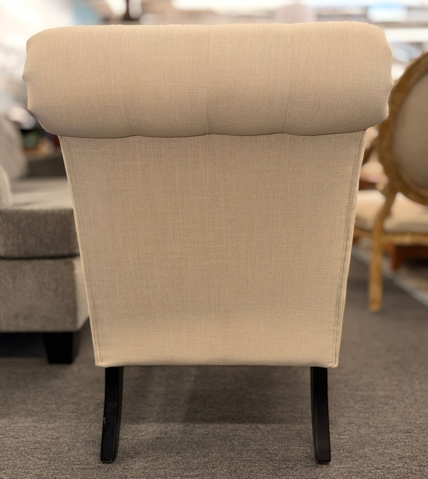 Button tufted slipper chair upholstered in cream textured fabric with an armless design, turned wooden front legs, and decorative casters.