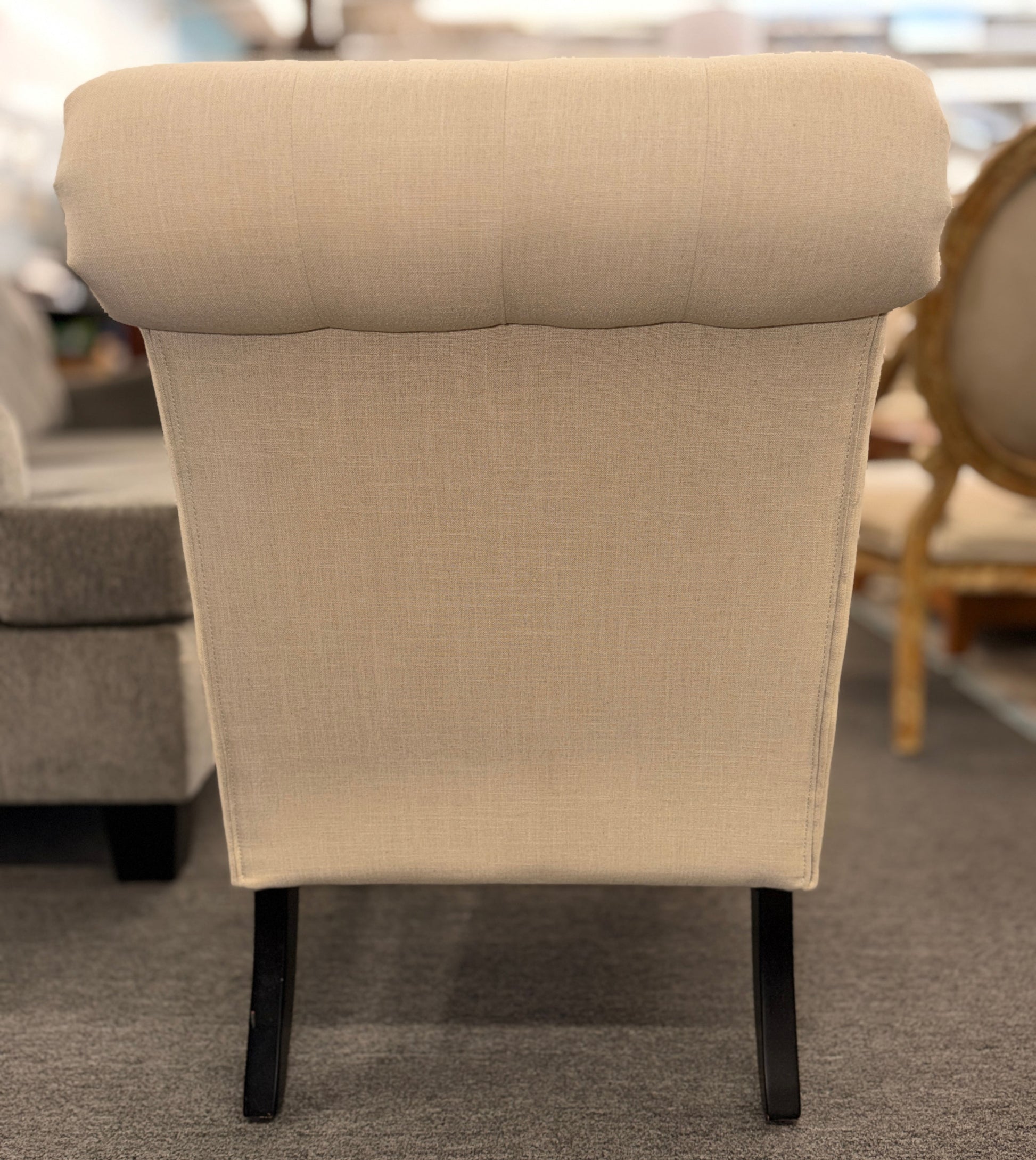 Button tufted slipper chair upholstered in cream textured fabric with an armless design, turned wooden front legs, and decorative casters.