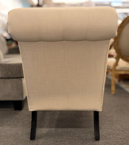 Button tufted slipper chair upholstered in cream textured fabric with an armless design, turned wooden front legs, and decorative casters.