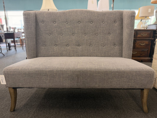 Transitional button tufted high wingback loveseat settee featuring gray upholstered fabric and dark wood legs in a showroom setting at 2nd Debut Houston consignment showroom