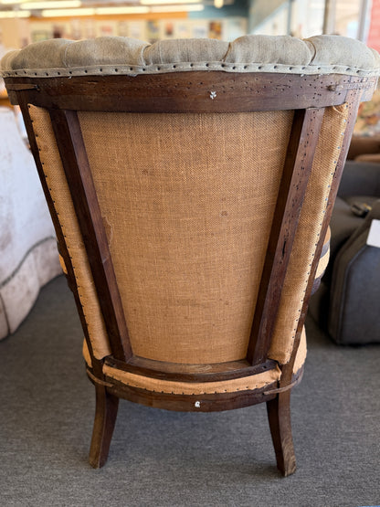 A classic wingback armchair featuring a beige channel-tufted fabric back, distressed brown leather seat cushion, dark wooden legs, and decorative nailhead trim.